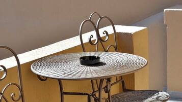 A metal table and chairs on an outdoor balcony with a beige wall and tiled floor.
