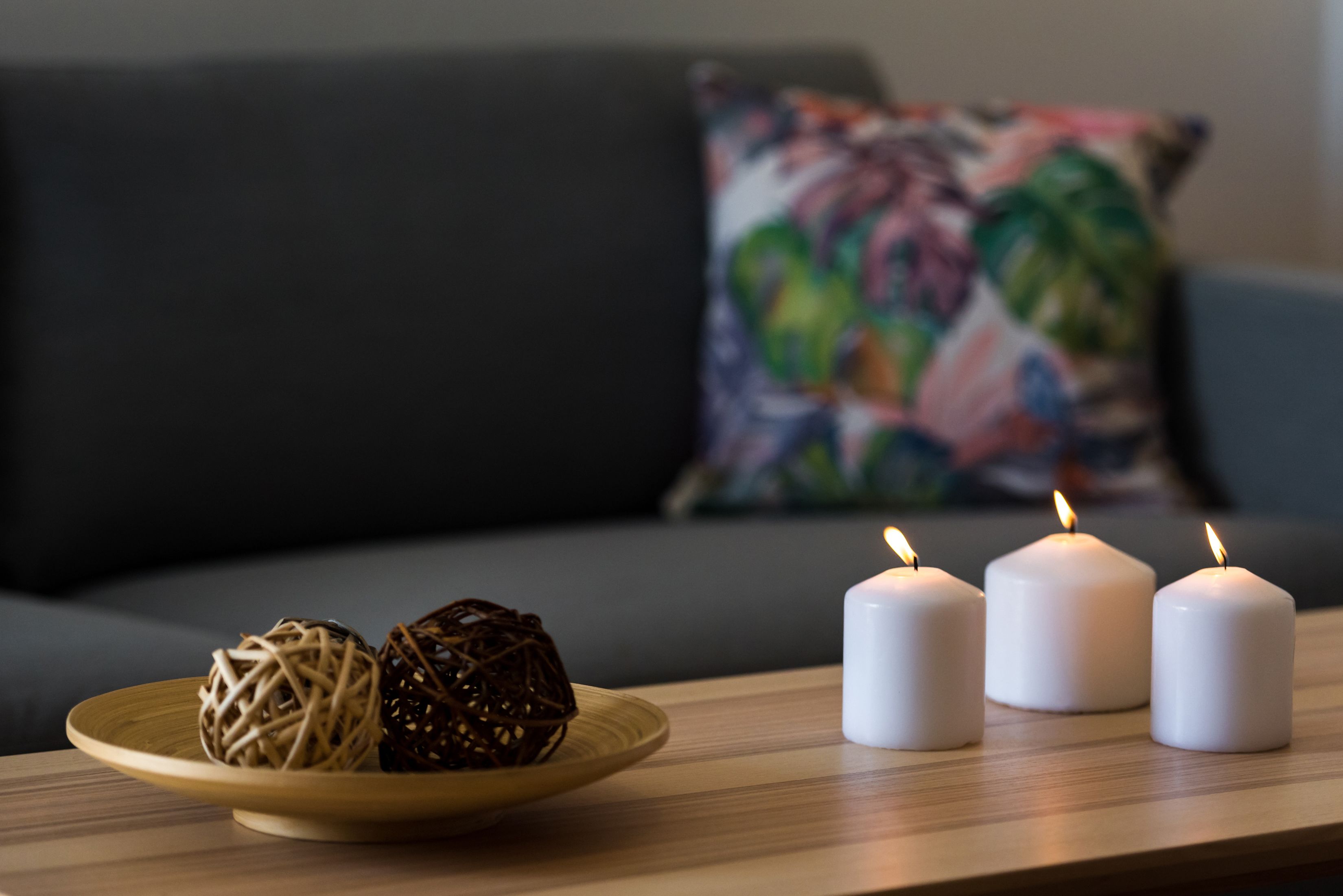 Una mesa de madera con tres velas blancas y dos bolas decorativas sobre un plato.