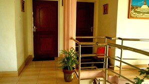 Un pasillo con puertas de madera, una planta en maceta y una escalera con barandilla de metal.