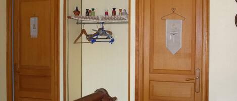 A room with two wooden doors, a bed with a red blanket, a shelf with toiletries, and a coat rack.