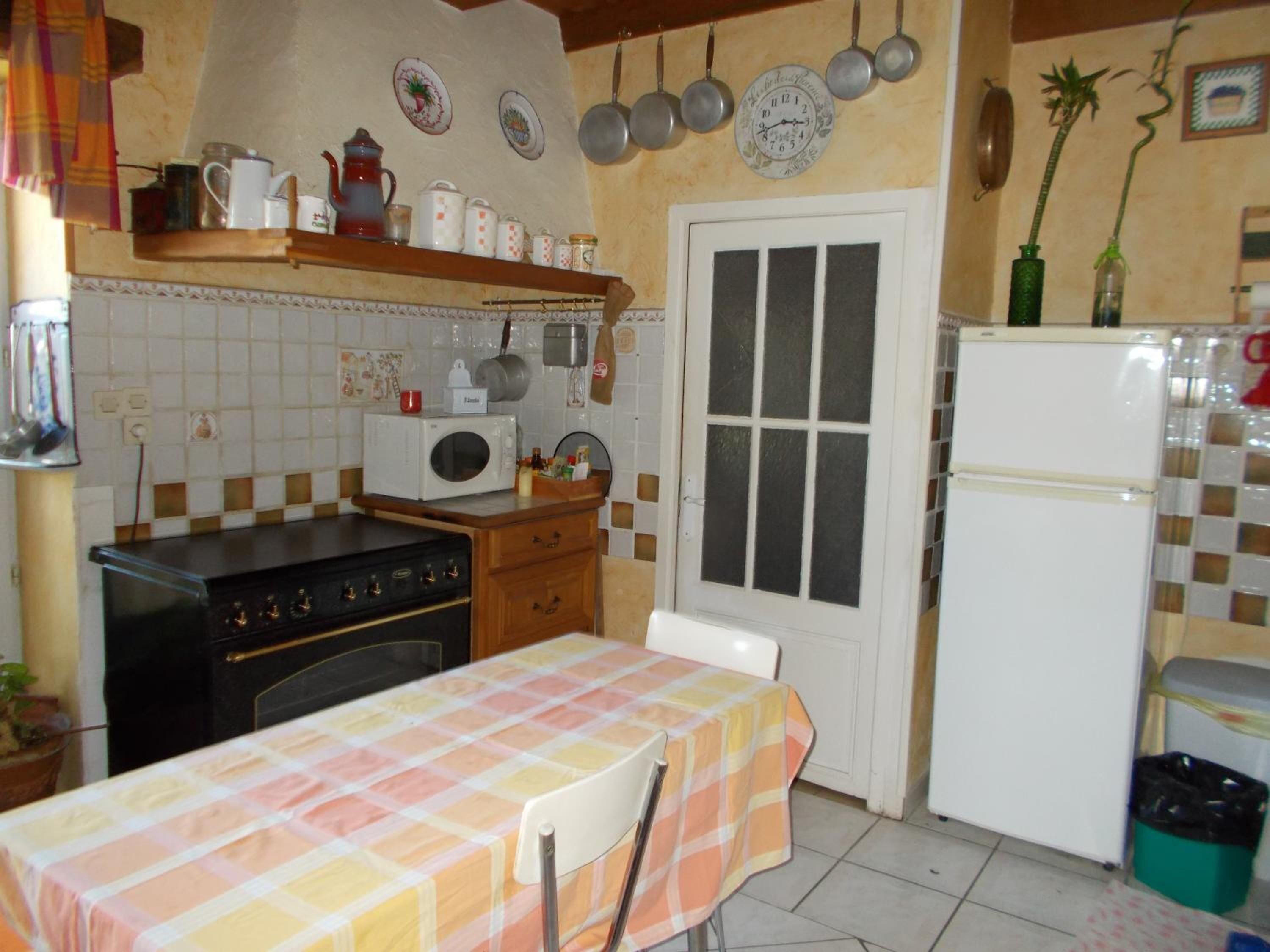 A kitchen with a stove, microwave, refrigerator, and a table with a checkered tablecloth.