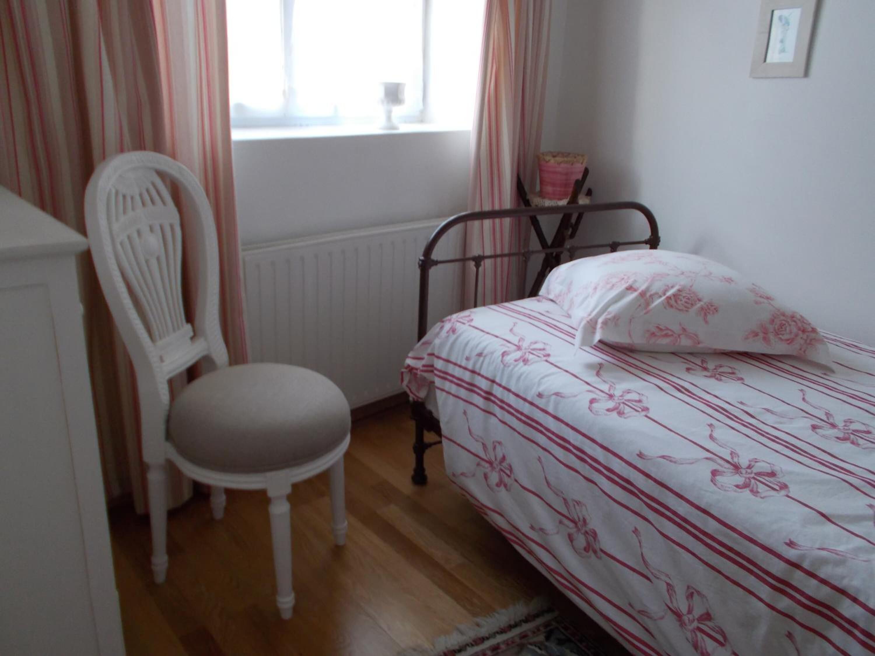 A bedroom with a bed, a chair, a radiator, and a window with curtains.