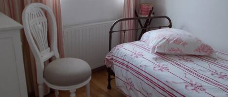 Ein Schlafzimmer mit einem Bett, einem Sessel, einem Heizkörper und einem Fenster mit Vorhängen.