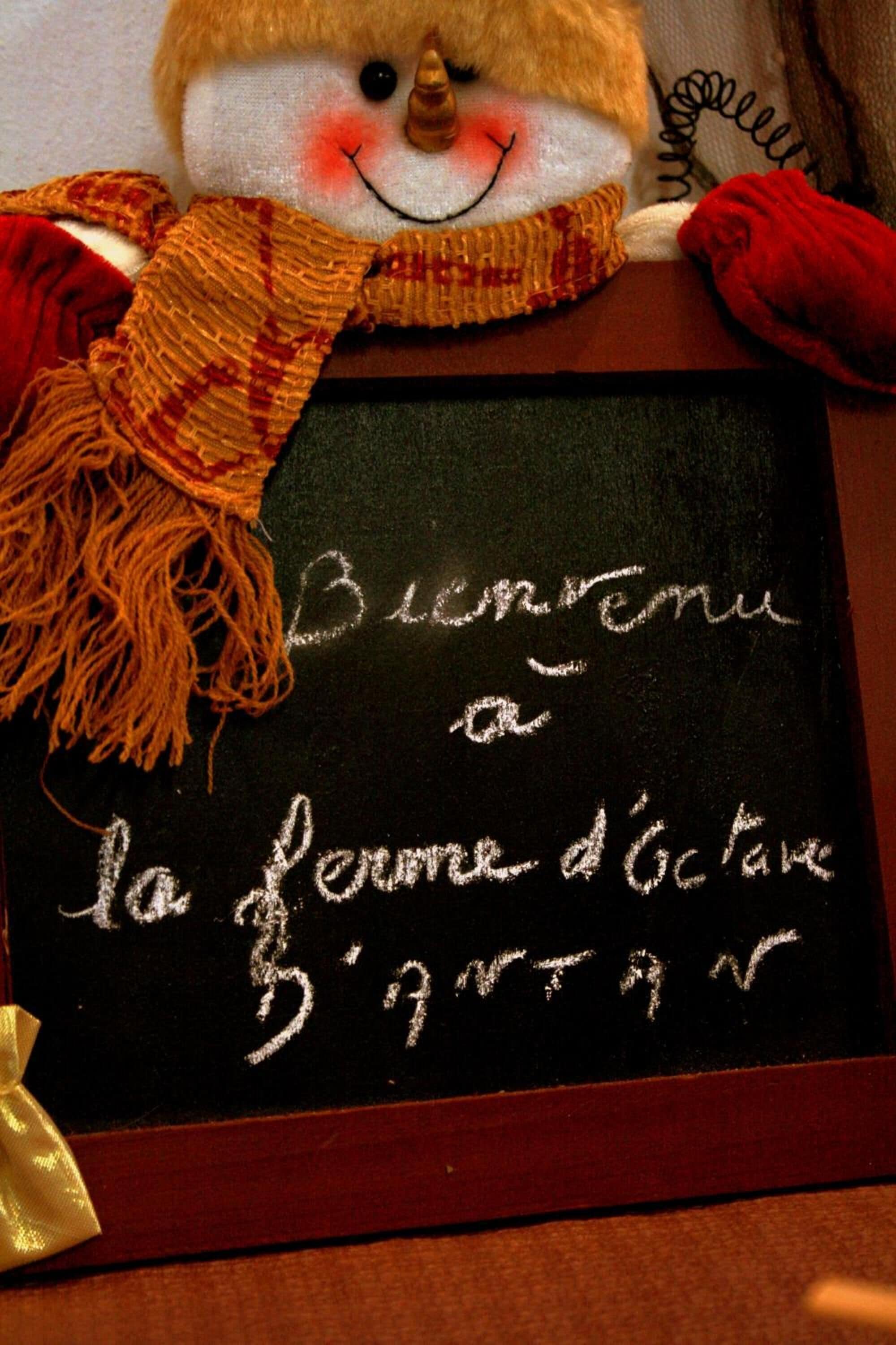 A chalkboard with the message "Bienvenue a la ferme d'octave" and a snowman decoration.