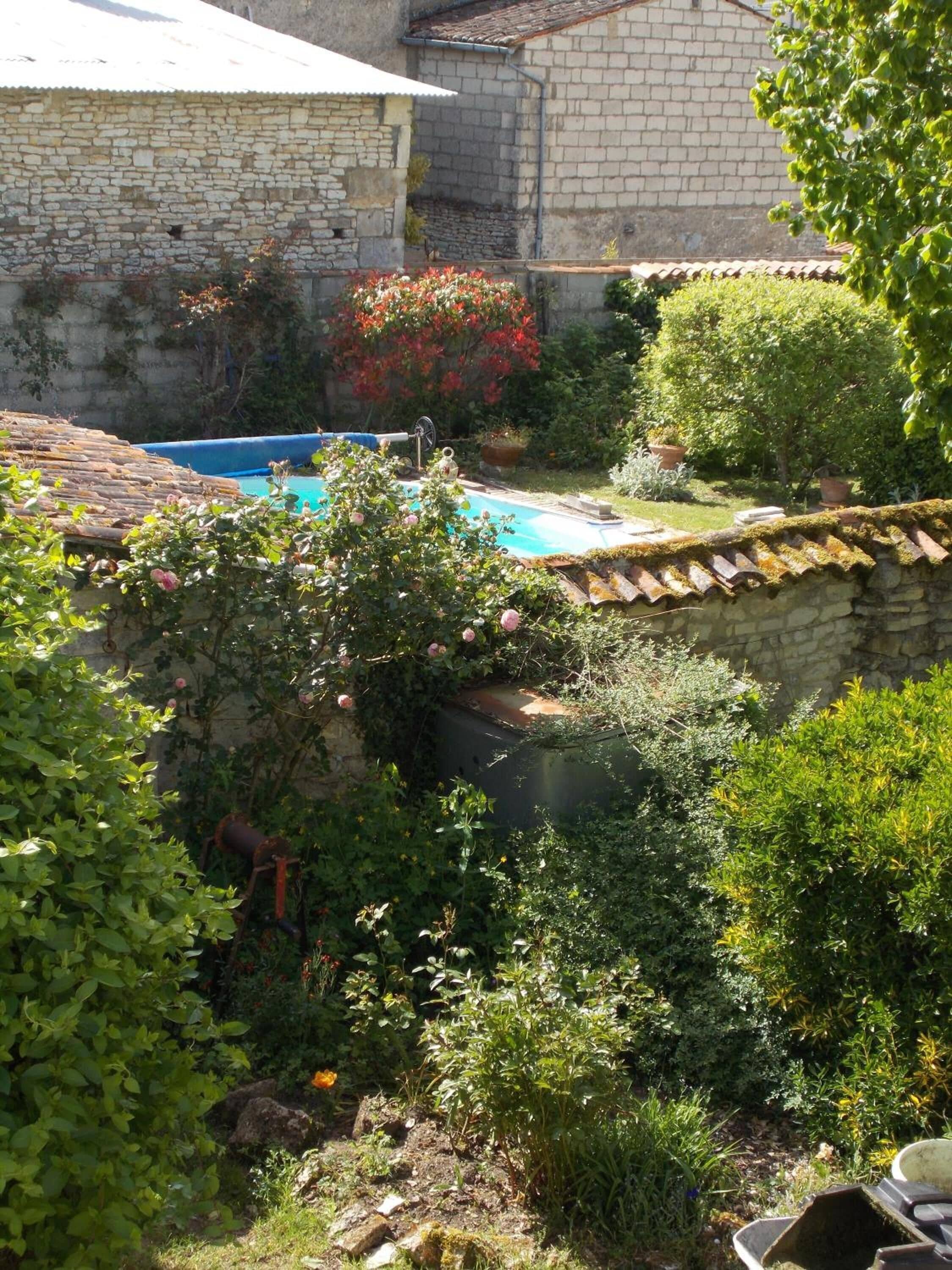A courtyard with a swimming pool, stone walls, and various plants.