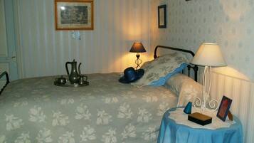 Un dormitorio con cama, una mesita de noche con lámpara, una pequeña mesa con un marco de fotos y una pared decorada con un cuadro.