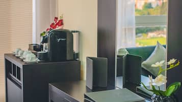 Quarto de hotel com escrivaninha, cafeteira, um vaso de flores e vista para a cidade através de uma janela ampla.