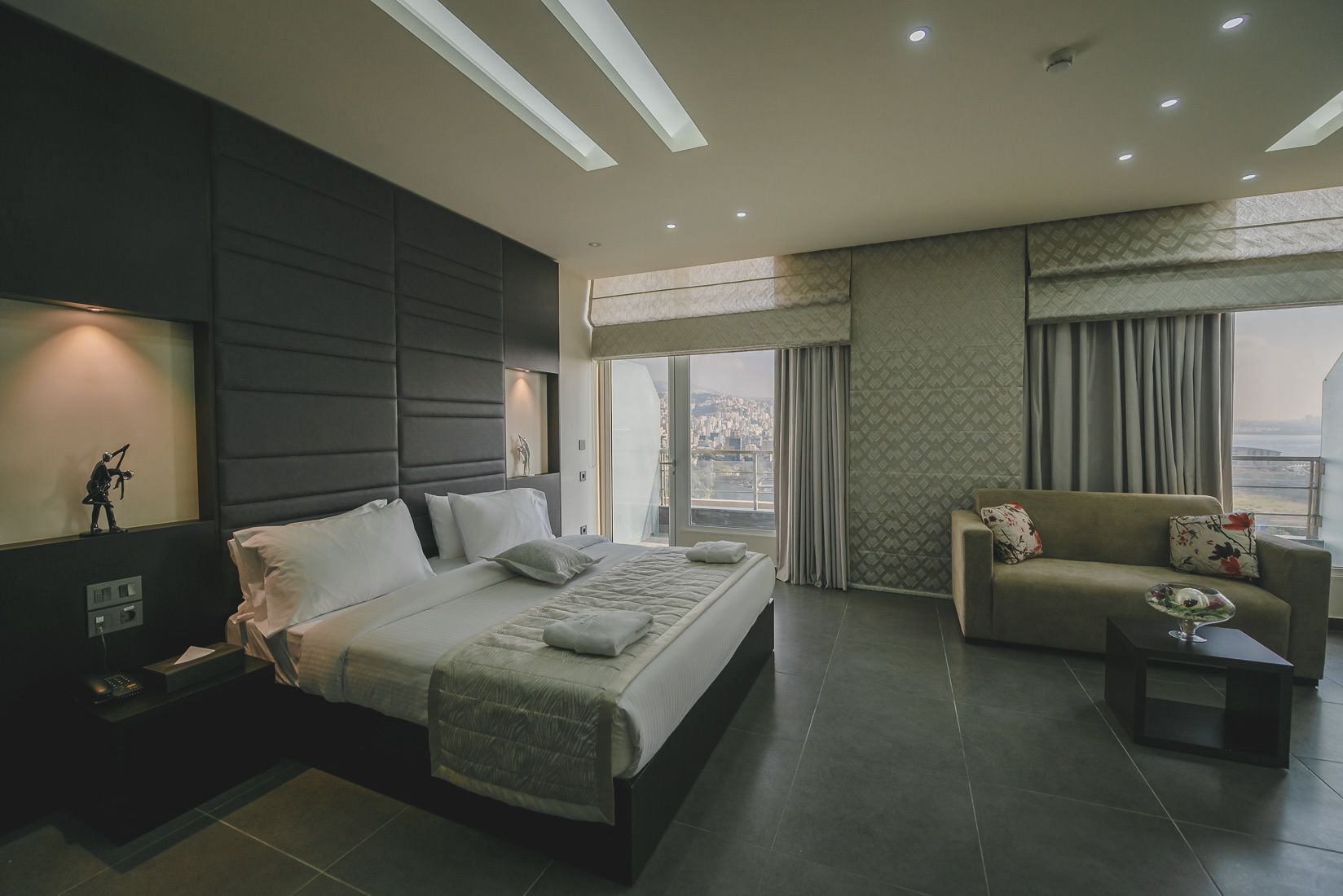 A modern hotel room with a large bed, a sofa, and a view of the city.