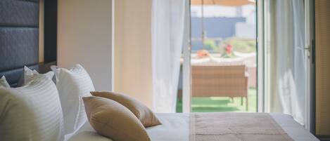 Habitación de hotel con cama, almohadas y vista a un área exterior con mesa y sombrilla.