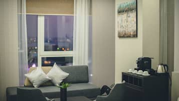 A modern living room with a grey sofa, two white pillows, a small table with a plant, and a coffee station.