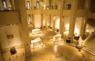Un interior espacioso con techos altos y columnas, que presenta un área central abierta con algunas estatuas y una escalera a la derecha.