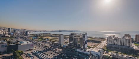 A cityscape with a large parking area, a prominent building with a billboard, and a view of the sea.