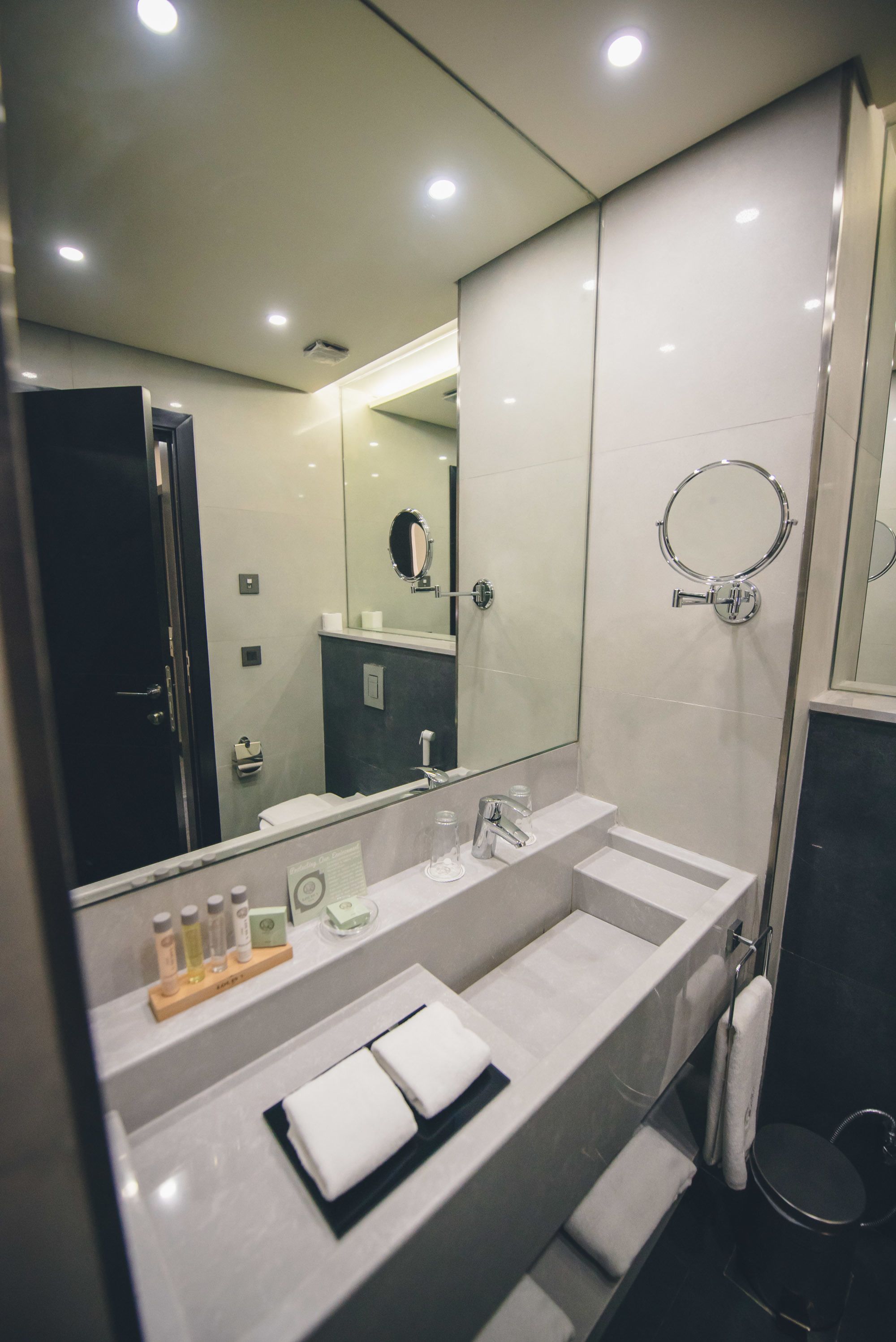 A modern bathroom with a large mirror, two sinks, and a shower area.