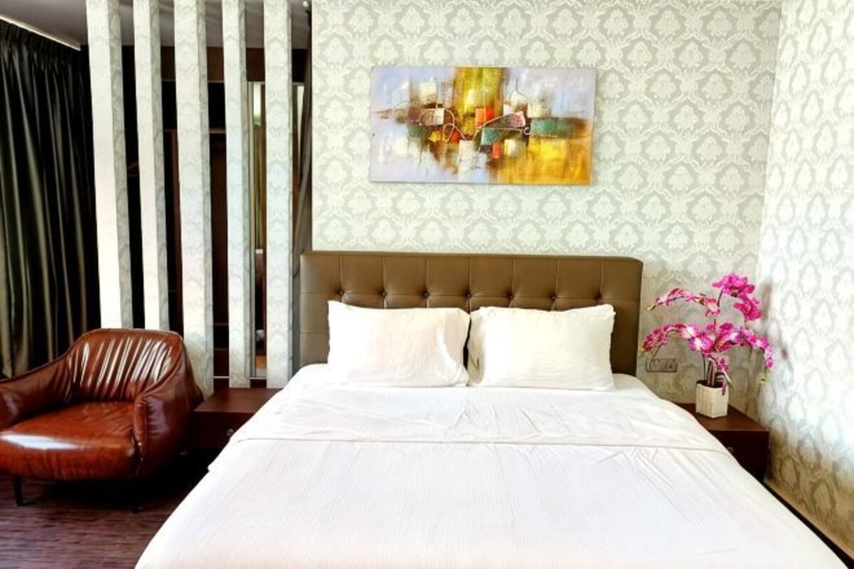 A hotel room with a large bed, a leather armchair, a nightstand with a vase of flowers, and a patterned wallpaper.