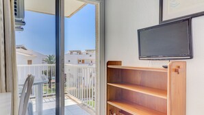 A room with a sliding glass door leading to a balcony, a wooden shelf unit, and a mounted television. - Apartamentos Llevant Puerto de Pollensa (Pollenca)