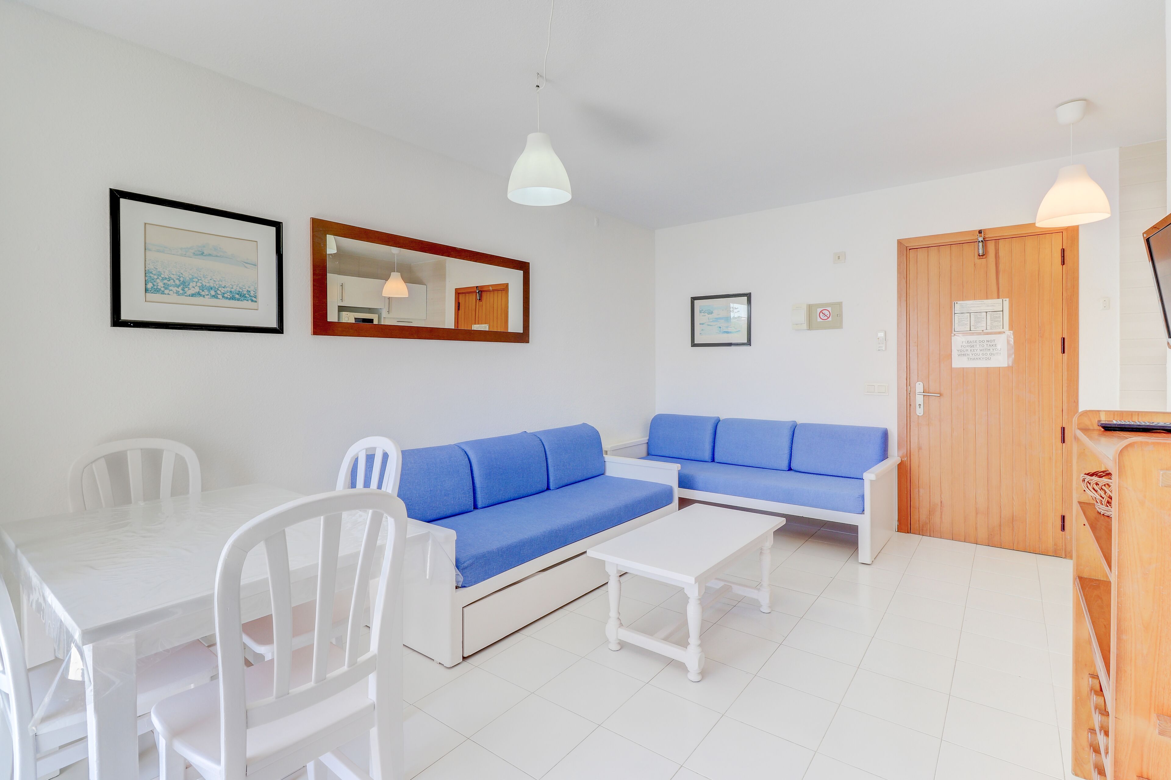 A room with a white table, two blue sofas, a white chair, a wooden door, and a mirror on the wall.