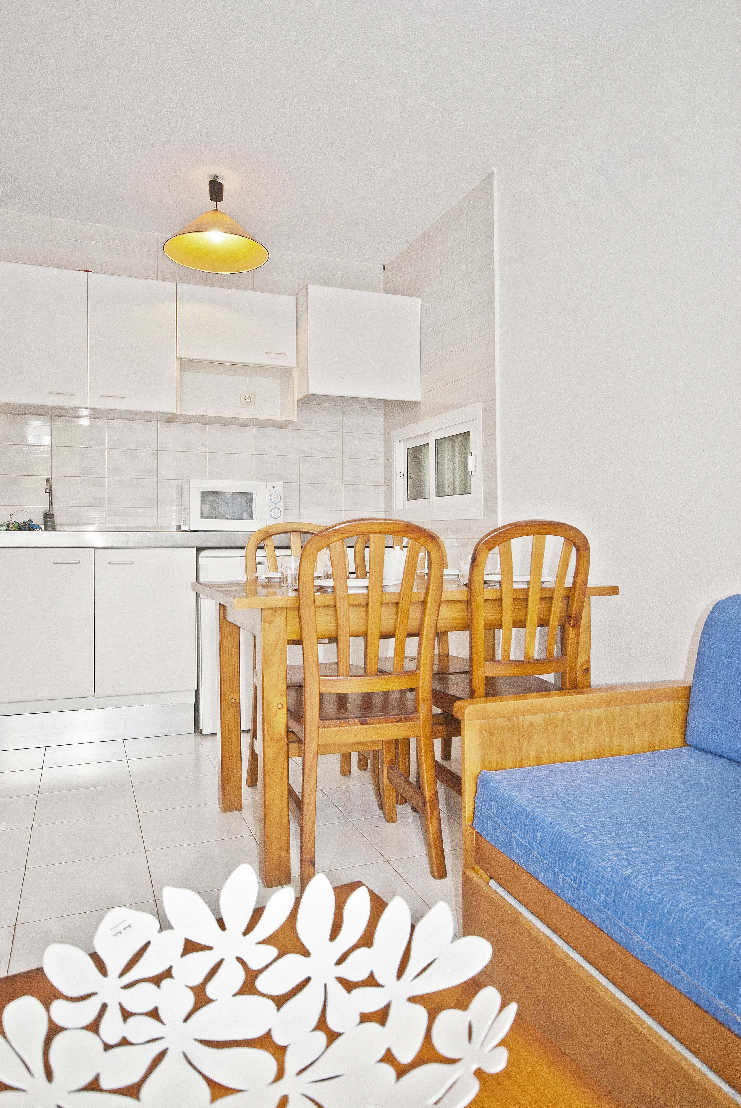 Cocina compacta con armarios blancos, microondas y una mesa de comedor con sillas.