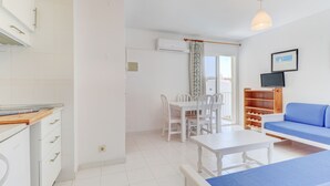 A modern, well-lit room with a dining table, chairs, a sofa, and a TV. - Apartamentos Llevant Puerto de Pollensa (Pollenca)