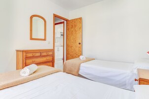 Habitación de hotel con dos camas, un aparador de madera, un espejo y una puerta que da a un balcón.