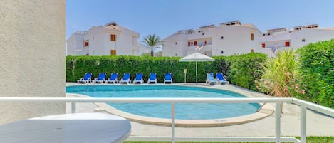 A swimming pool with blue lounge chairs, a white building with balconies, and a clear sky.