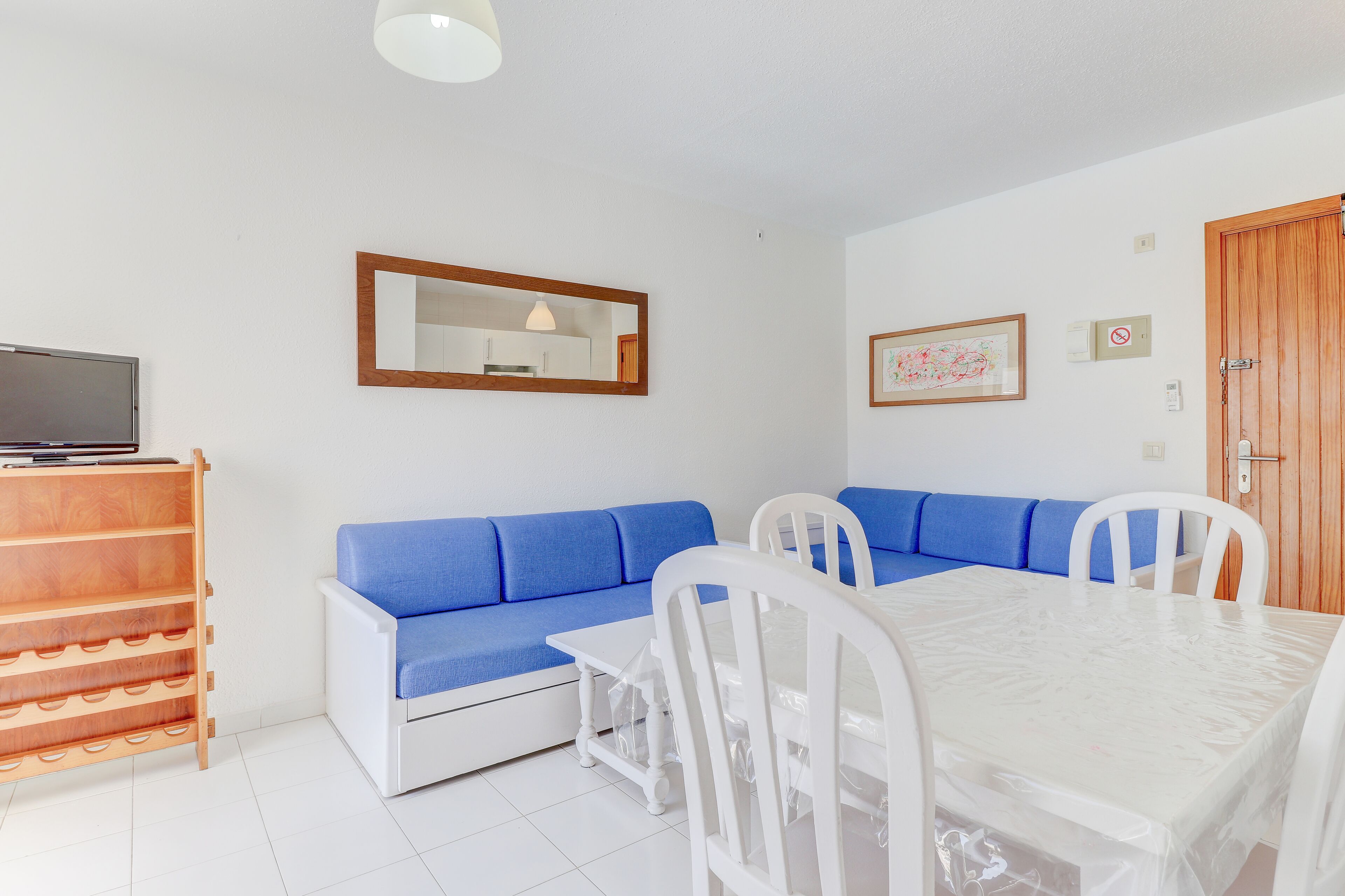 A room with a blue sofa, a white dining table, and a wooden cabinet with wine glasses.
