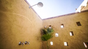 Een smalle binnenplaats met een waterornament, een palmp plant en een hanglamp.