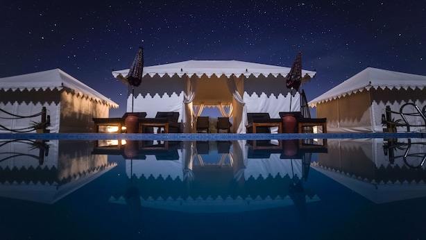 Een nachtzicht van een resort met een reflecterend zwembad, tenten en een heldere sterrenhemel.