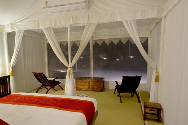 A bedroom with a bed, two chairs, a wooden chest, and a large window with curtains. - Dhora Desert Resort & Spa By Eight Continents (Balesar)