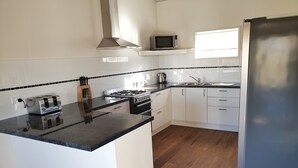 A modern kitchen with a central island, white cabinetry, a stainless steel range hood, a microwave, and a refrigerator. - Skytrek Willow Springs Station (Flinders Ranges)