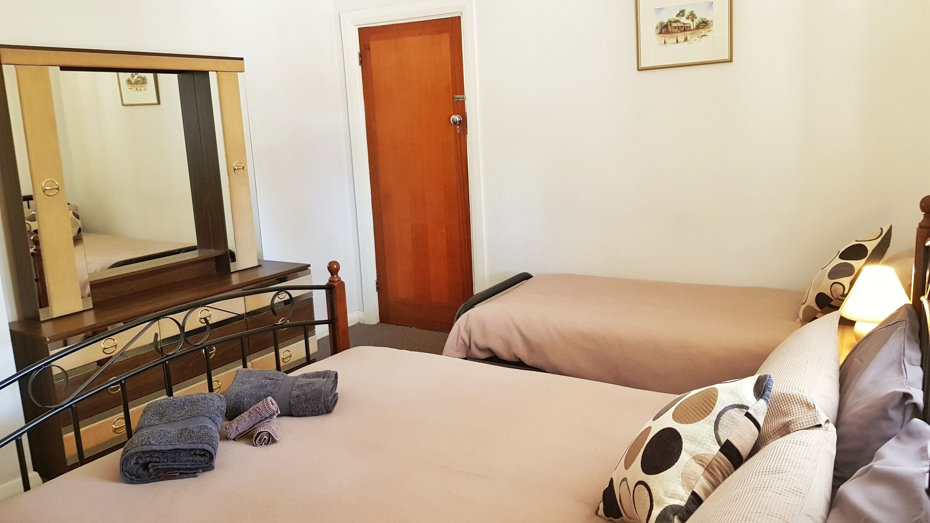 Un dormitorio con dos camas, una puerta de madera, un espejo y un cuadro en la pared.
