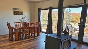 A room with a wooden dining table and chairs, a fireplace, and a large window with a view of the outdoors. - Skytrek Willow Springs Station (Flinders Ranges)