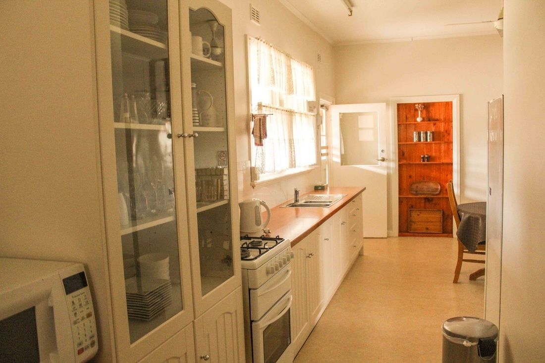 Een kleine keuken met witte kastjes, een fornuis en een spoelbak. Er is een eethoek met een tafel en stoelen.