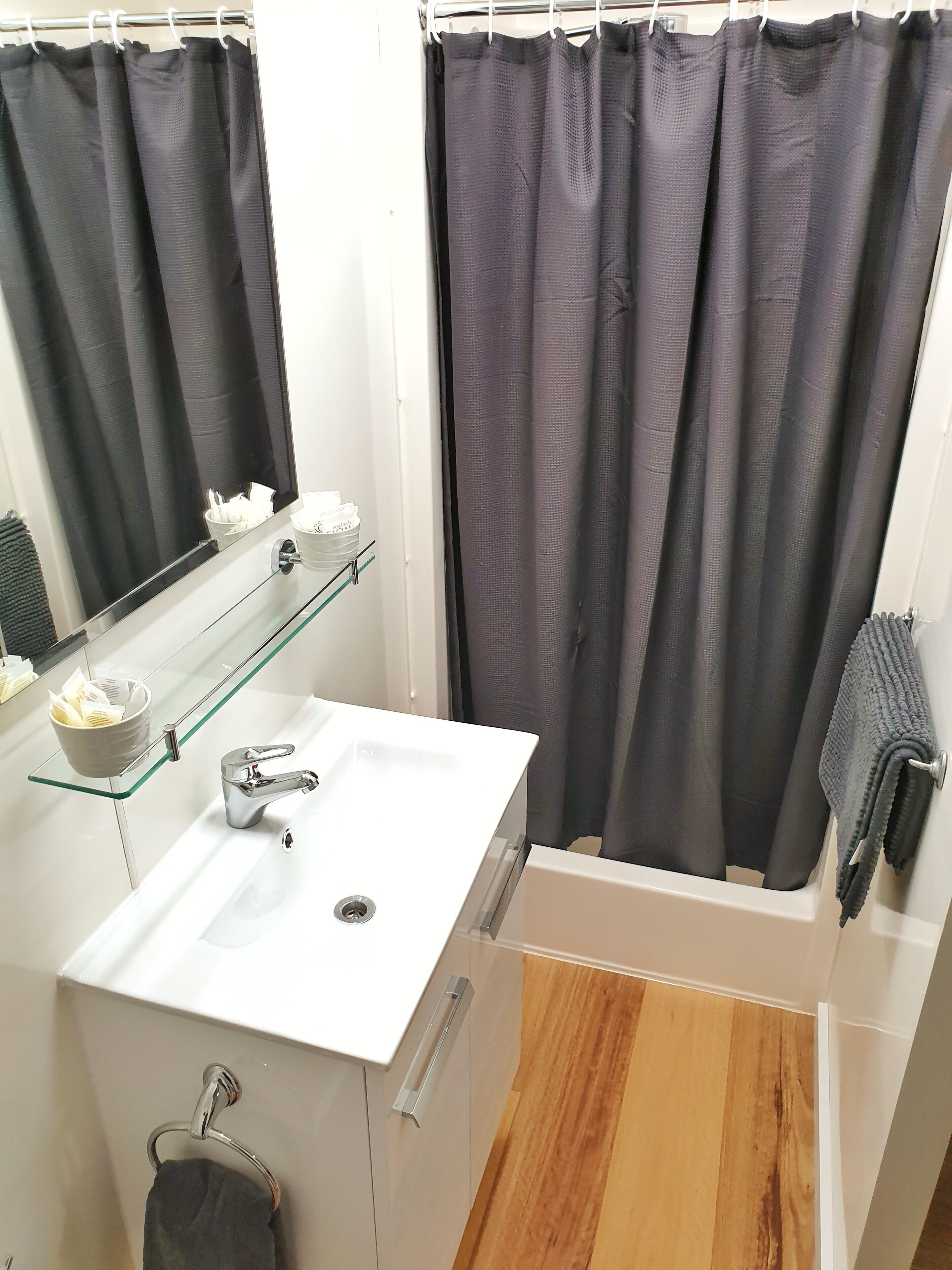 A modern bathroom with a white sink, glass shelf, and a bathtub.