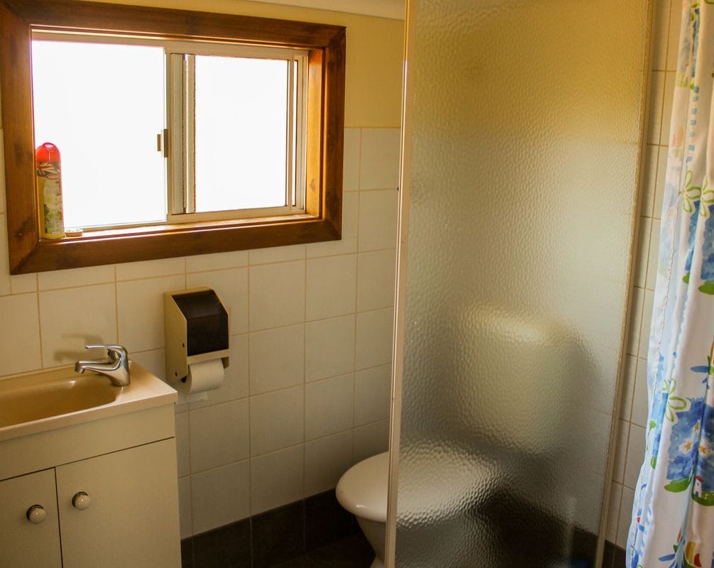 A bathroom with a window, a toilet, a sink, and a paper towel dispenser.
