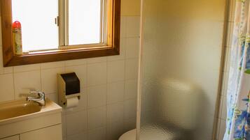 A bathroom with a window, a toilet, a sink, and a paper towel dispenser.
