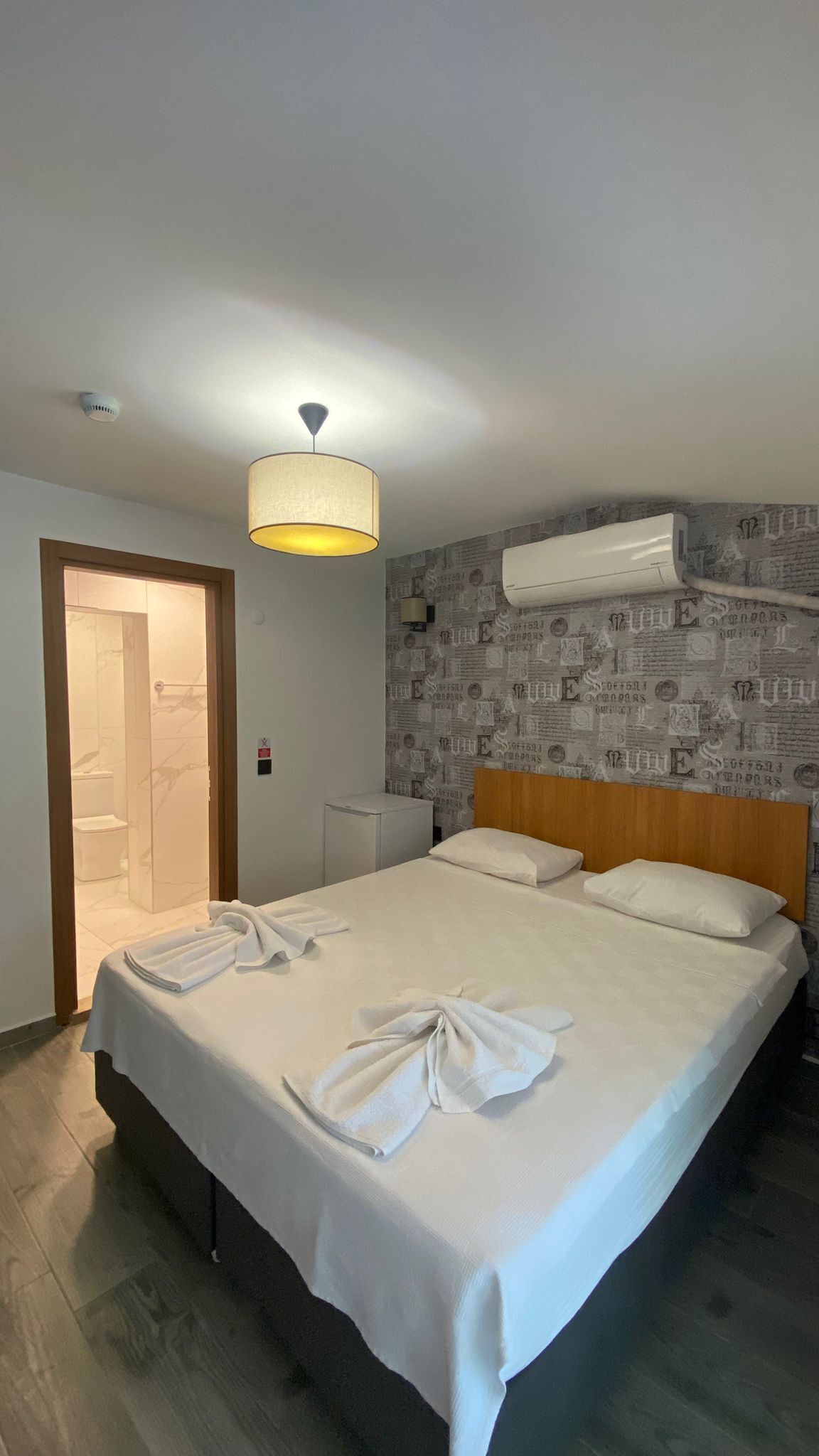 A hotel room with a bed, a shower, a ceiling fan, and a wall-mounted air conditioner.
