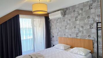Una habitación de hotel con cama, cabecero de madera, mesita de noche y ventana con cortinas.