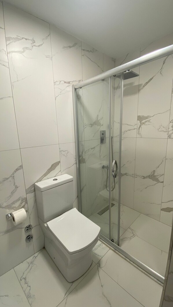 A bathroom with a toilet, a glass shower enclosure, and marble-patterned walls. - Kerpe Kaptan Pansiyon (Kandira)