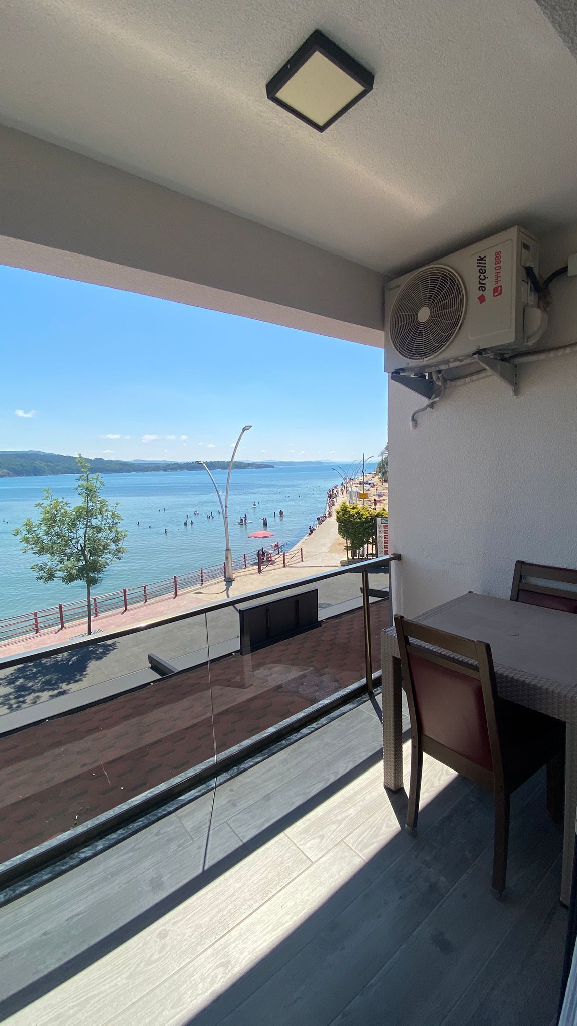 Un balcón con vista a la playa, una mesa y un equipo de aire acondicionado.