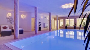 A modern indoor swimming pool with a clear water surface, surrounded by spa chairs and potted plants. - Wellnesshotel Auszeit (Achslach)