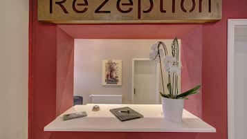 A reception desk with a sign reading "Rezeption" above it, a potted orchid, and a framed picture on the wall.