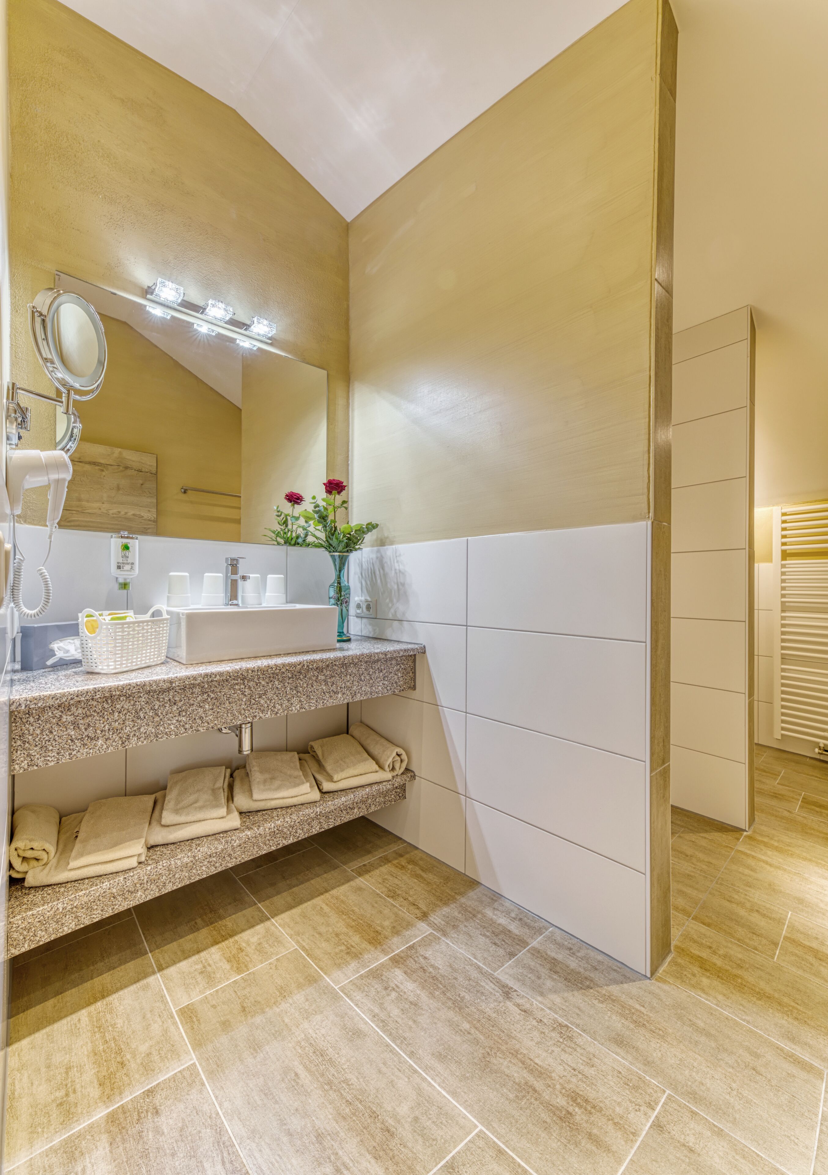 A bathroom with a granite countertop, a mirror, a vanity, a towel rack, and a vase with flowers.