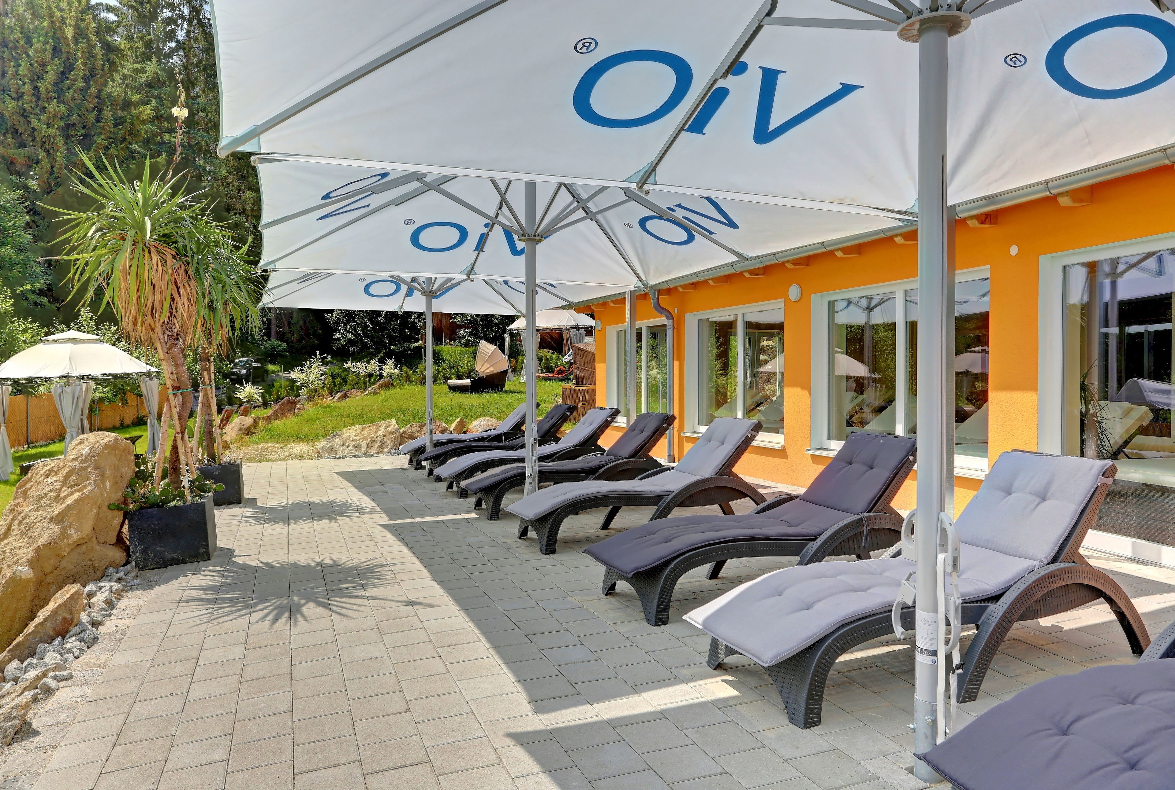 A row of sun loungers under white umbrellas with the logo "OIV" on a tiled patio area.
