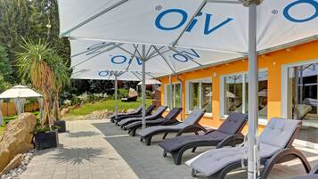 Una hilera de tumbonas bajo sombrillas blancas con el logotipo "OIV" en una zona de patio empavedada.