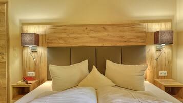 A double bed with two pillows, wooden headboard, bedside tables with lamps, and a small nightstand with a book.