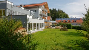A modern building with a glass facade, a balcony, and a solar panel roof. - Wellnesshotel Auszeit (Achslach)
