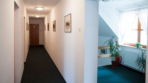 Ein Flur mit gerahmten Bildern an den Wänden, einem Blumentopf und einem Fenster mit Vorhängen.
