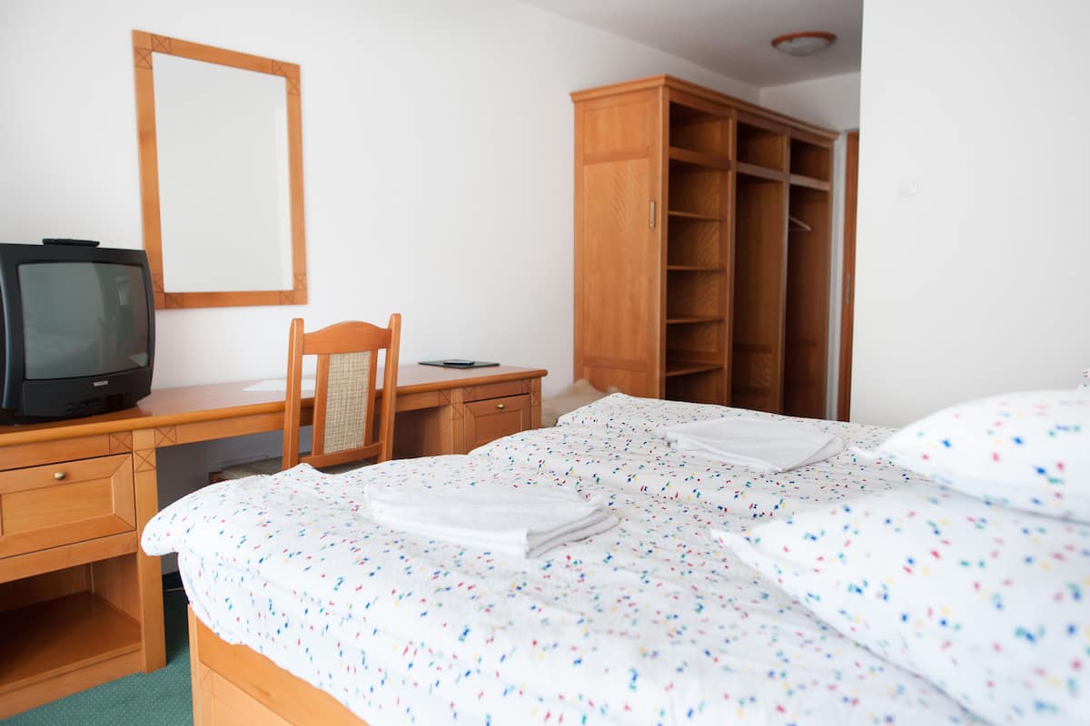 A hotel room with a bed, a desk with a television, a chair, and a wardrobe.