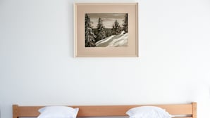 Ein Schlafzimmer mit einem hölzernen Kopfende, weißer Bettwäsche und einem gerahmten Gemälde einer verschneiten Landschaft an der Wand.