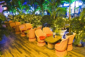 Una fila de sillas y mesas a rayas en un espacio interior bien iluminado, con plantas en macetas e iluminación ambiental.
